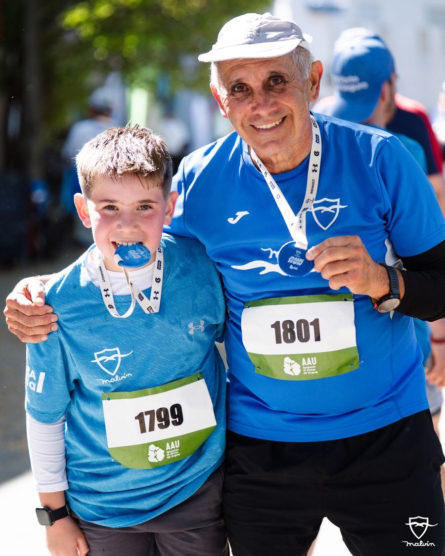 Un abuelo y su nieto posan con sus pecheras y medallas en la llegada