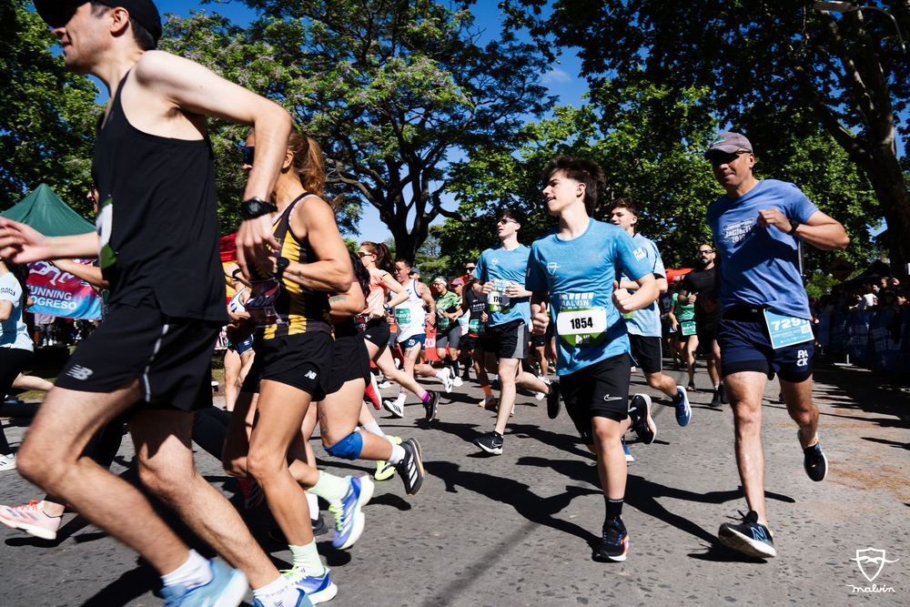 Pelotón de corredores de Malvín Run 2025 avanzando por una calle arbolada del barrio